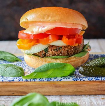 Lentil burger with toppings alongside baby spinach leaves and a pickle.