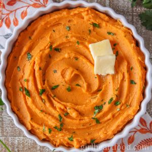 Dish of whipped sweet potatoes garnished with parsley and butter.