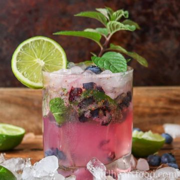 Glass of blueberry mojito garnished with mint and lime.