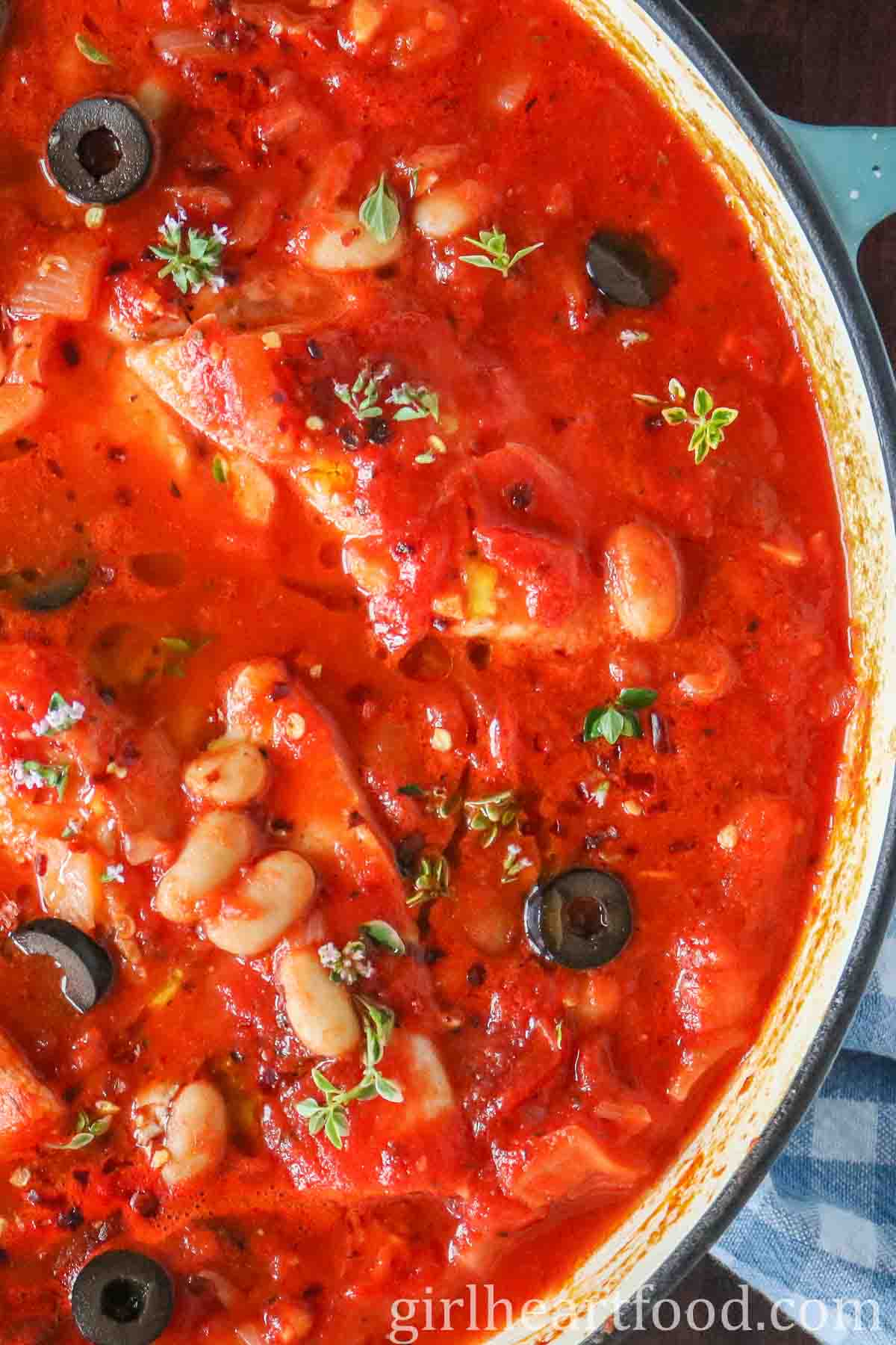 Close-up of a pan with cod poached in tomato sauce.