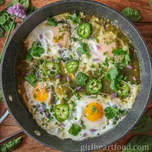 Pan of eggs in salsa verde garnished with toppings