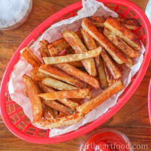 Basket of baked fries next to a dish of ketchup.