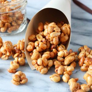 Honey roasted peanut clusters spilling out of a paper cone and onto a marble board.