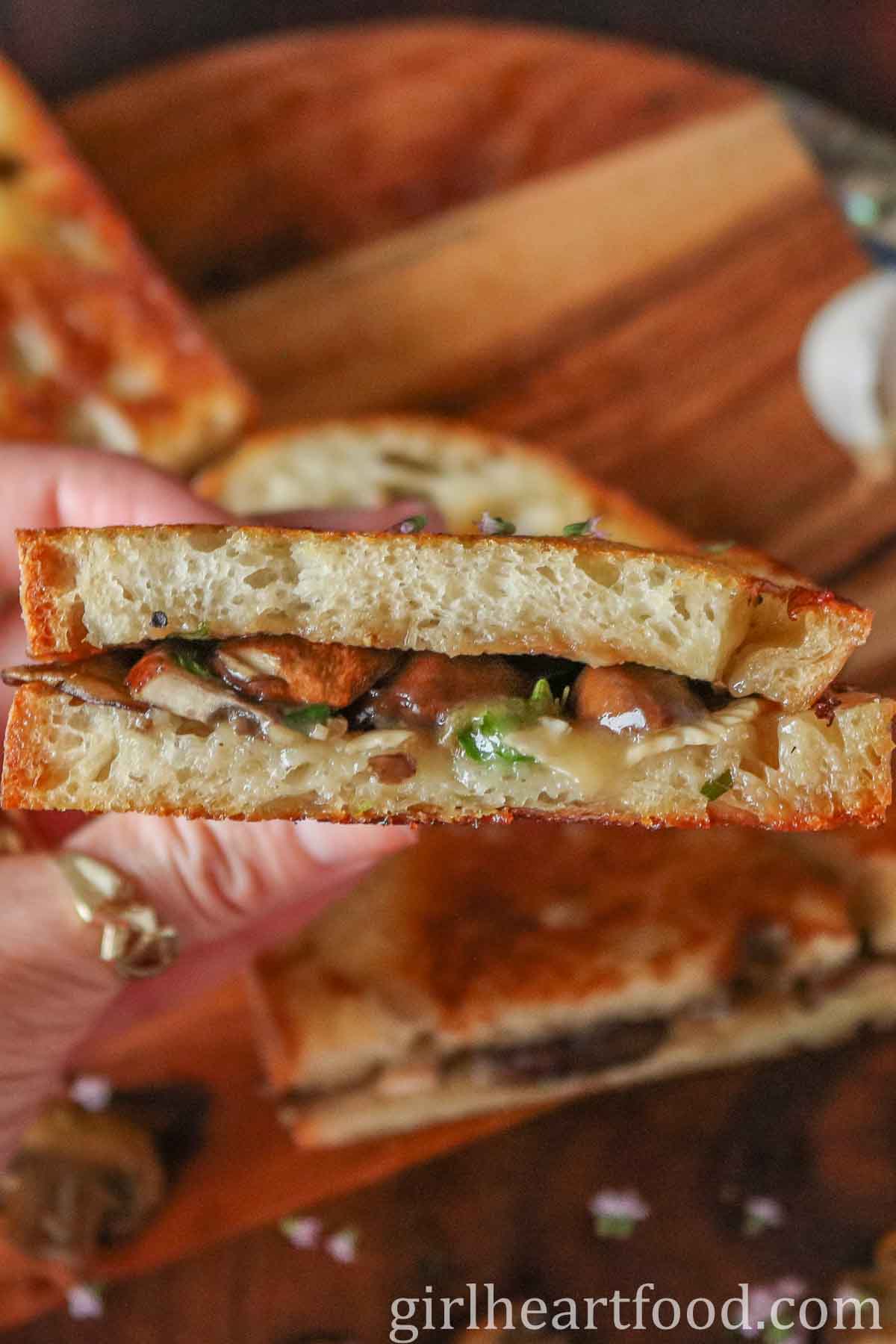 Hand holding half of a mushroom and Brie grilled cheese sandwich.
