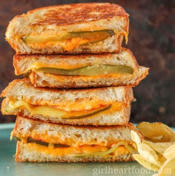 Stack of four pickle grilled cheese sandwich halves next to chips.