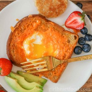 Egg-in-a-hole toast (with the yolk broke) and a gold fork resting on top of it.