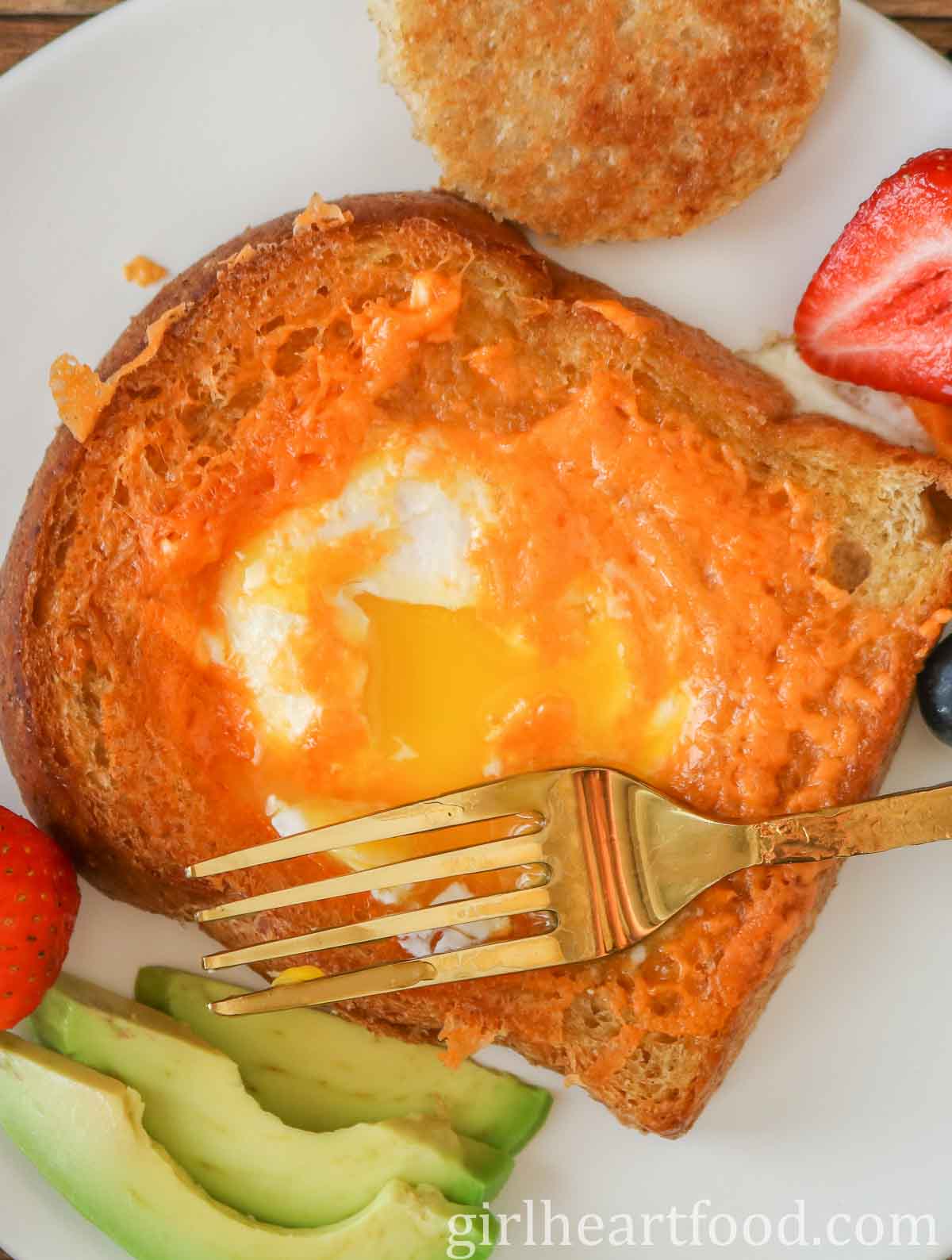 Egg-in-a-hole toast (with the yolk broke) and a gold fork resting on top of it.