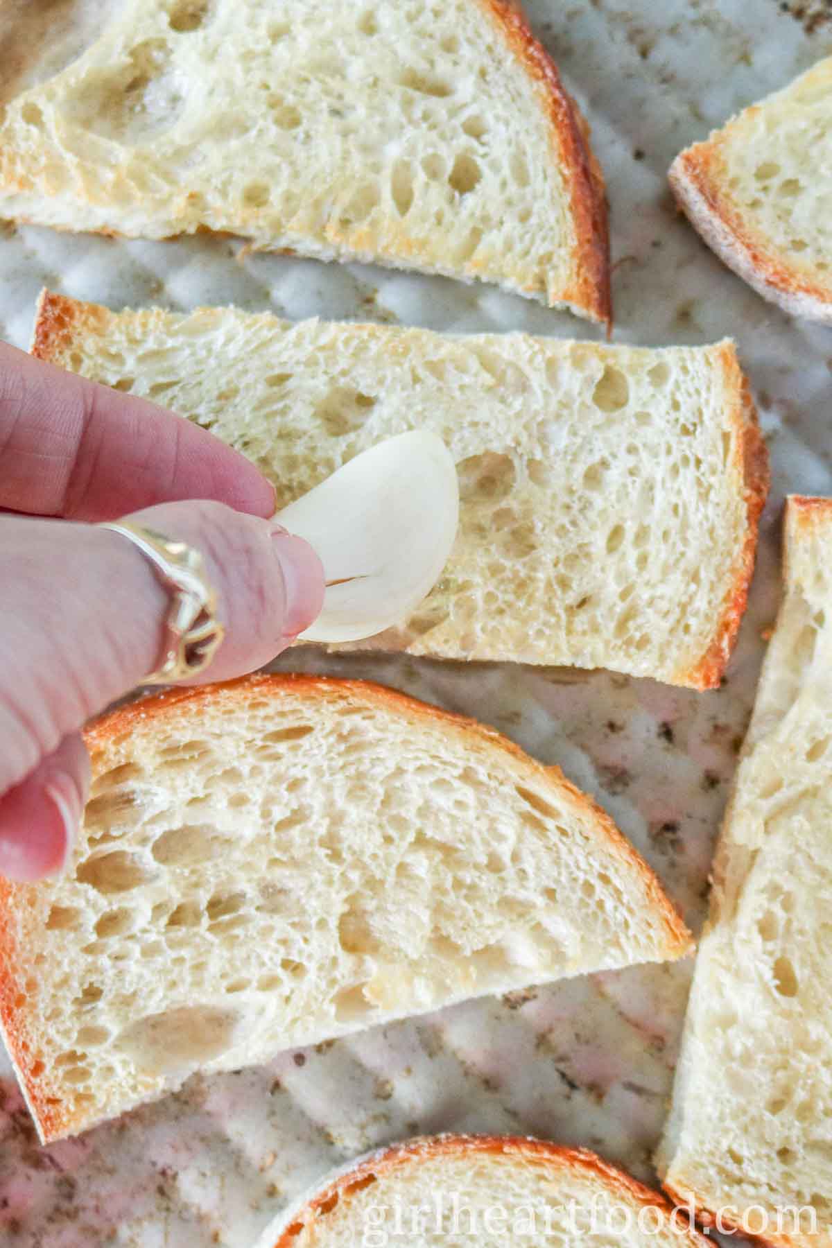 Hand rubbing a clove of garlic over a piece of crusty bread.