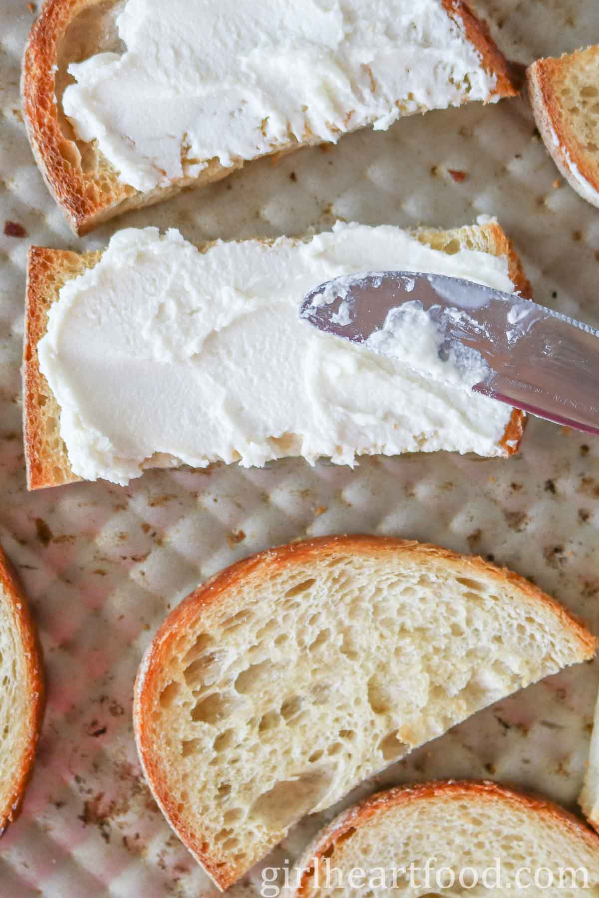 Spreading goat cheese on a piece of crusty bread with a butter knife.