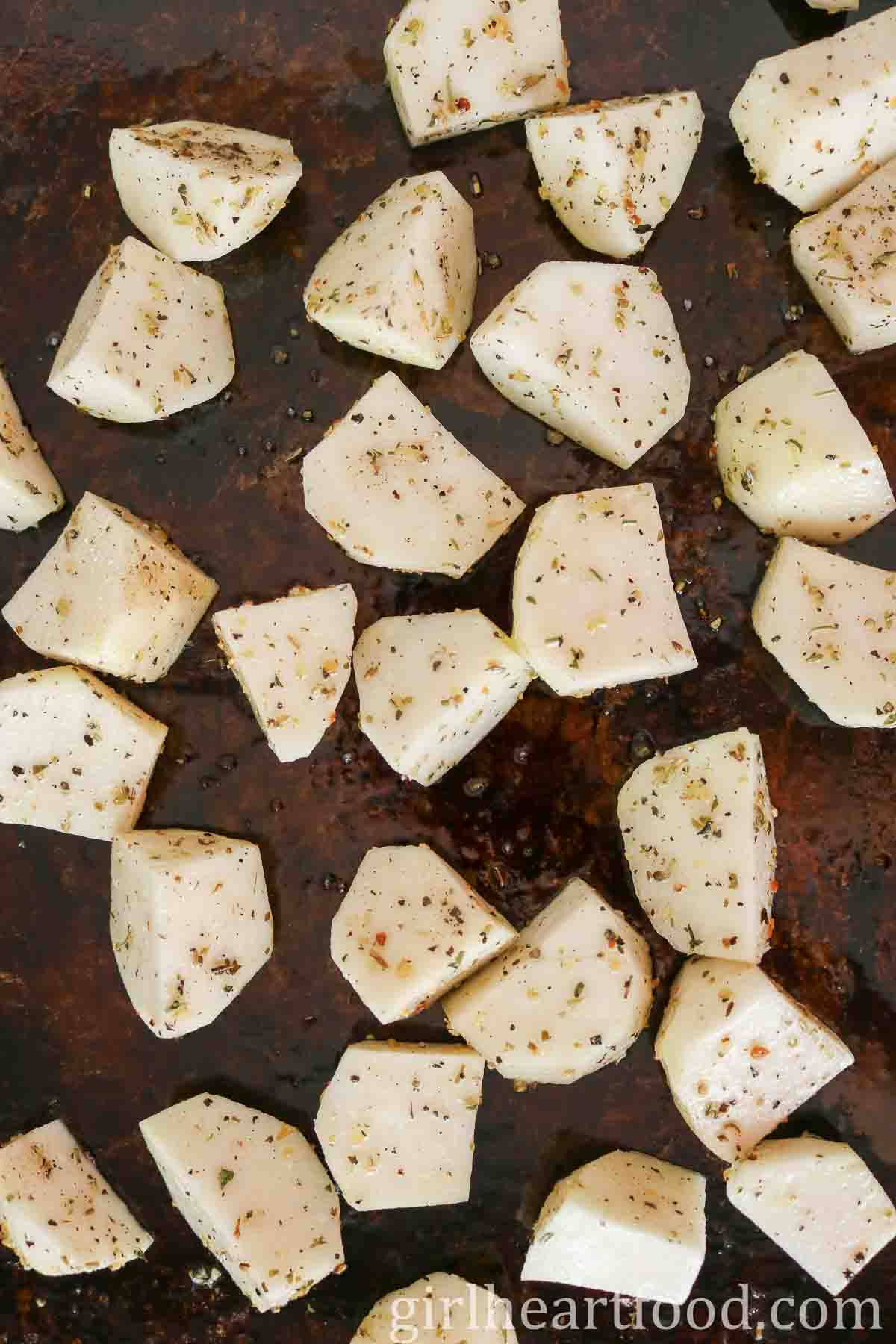 Uncooked chunks of kohlrabi with herbs on a sheet pan.
