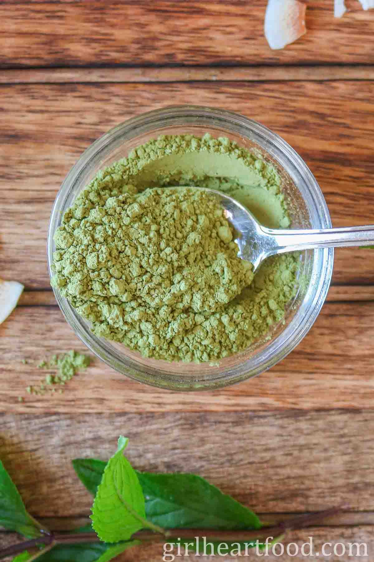 Small glass dish of matcha green tea powder with a spoon in the powder.