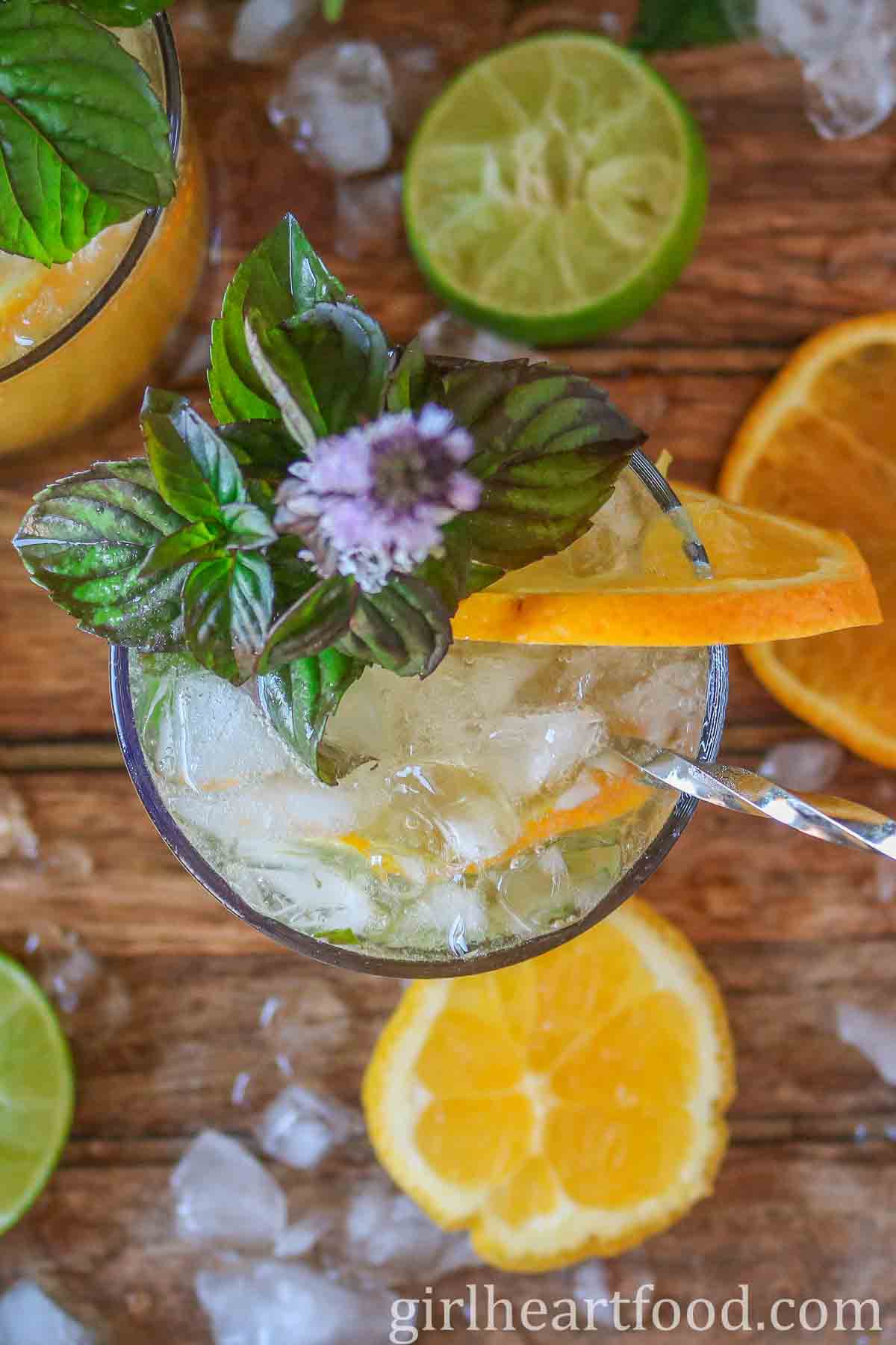 Glass of orange mojito with a stirrer garnished with mint and an orange slice.