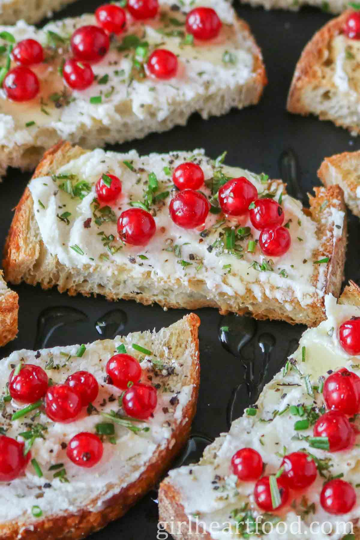 Goat cheese and red currant crostini on a black plate.