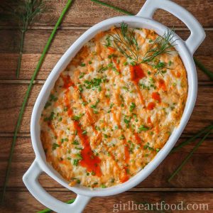 Buffalo dip in a baking dish garnished with chives, dill and buffalo sauce.