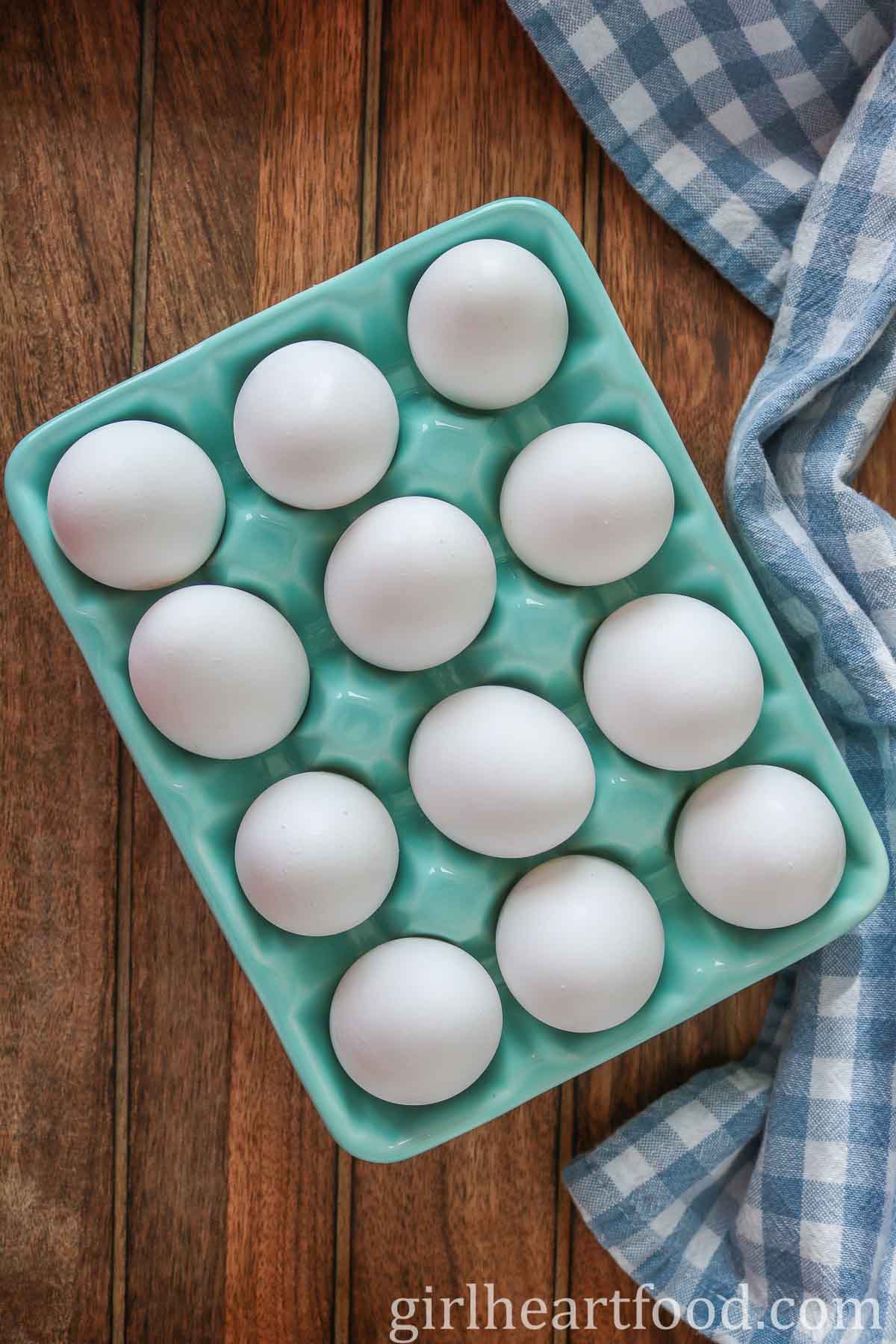 Glass cartoon of a dozen eggs next to a blue and white checkered tea towel.