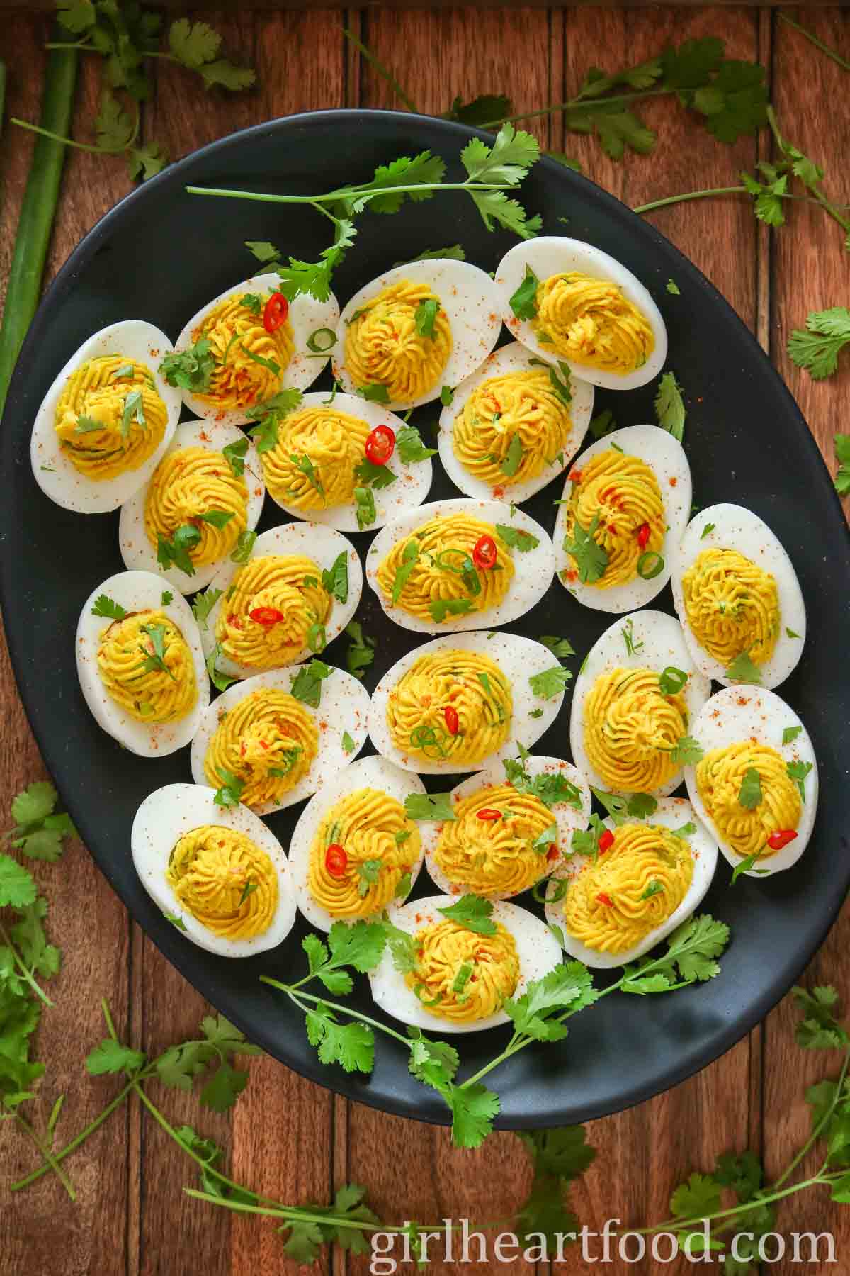 Curried deviled eggs on a black platter, surrounded by cilantro.