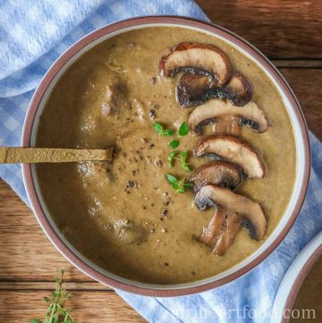 Bowl of mushroom soup garnished with mushrooms, thyme, black pepper and oil.