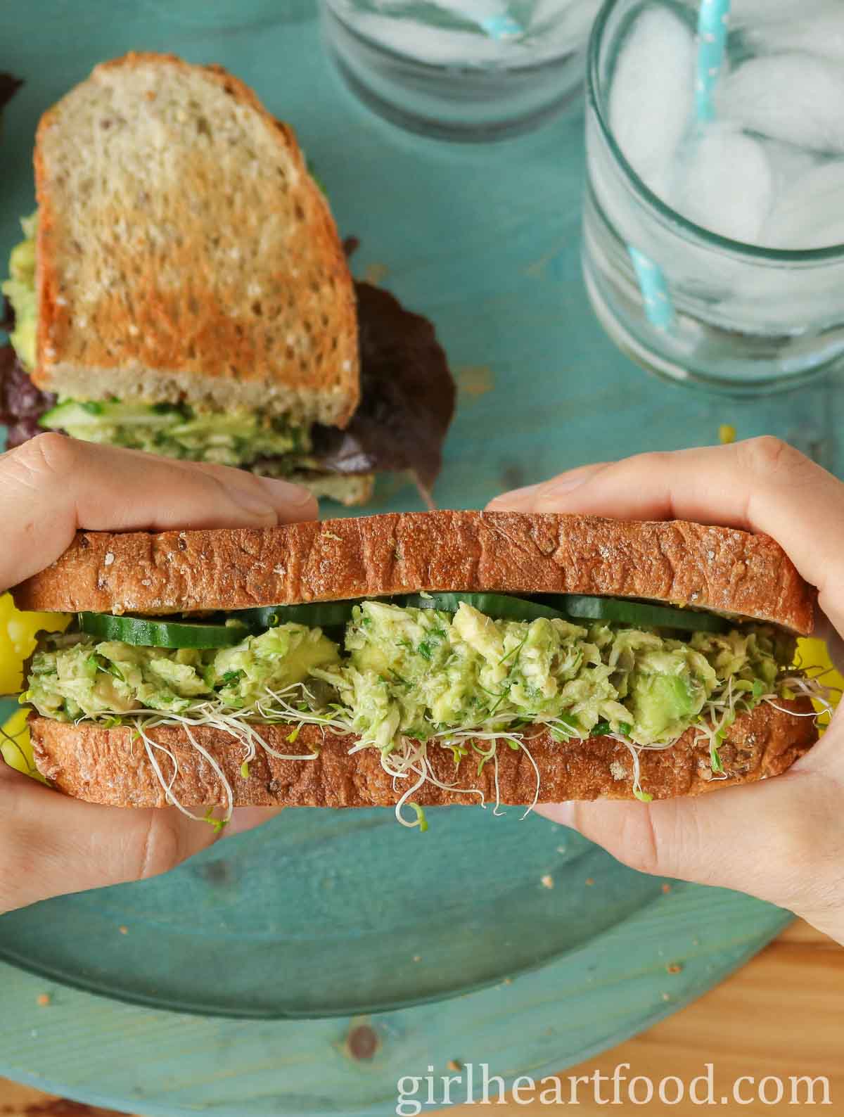 Two hands holding a tuna avocado salad sandwich.