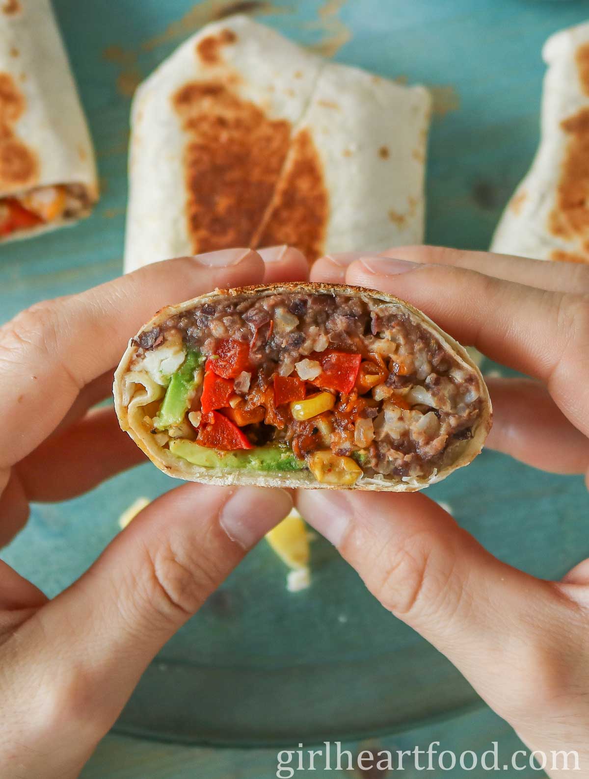 Two hands holding a refried bean burrito.