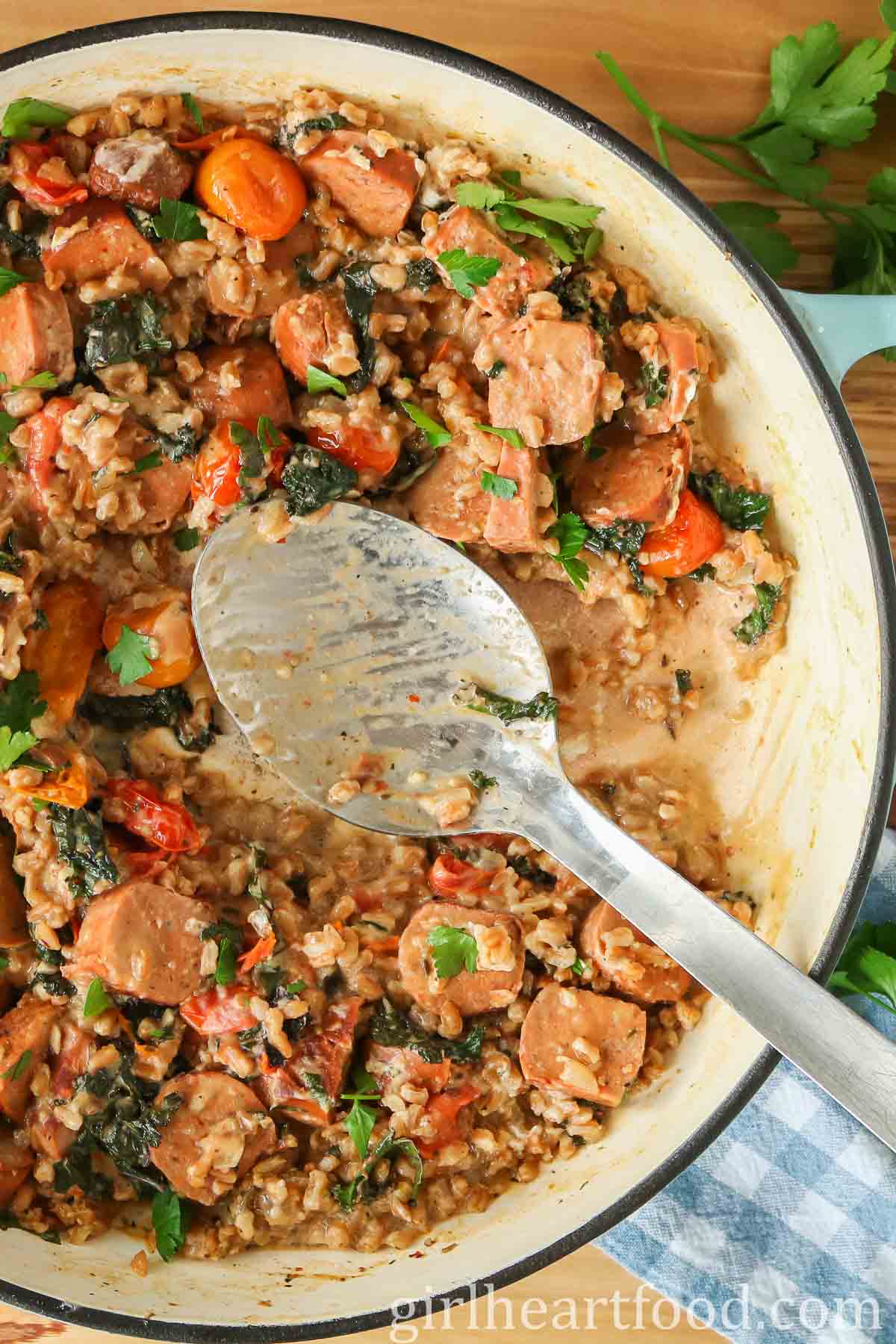 Farro, sausage and vegetables in a pan with a serving spoon resting in it.