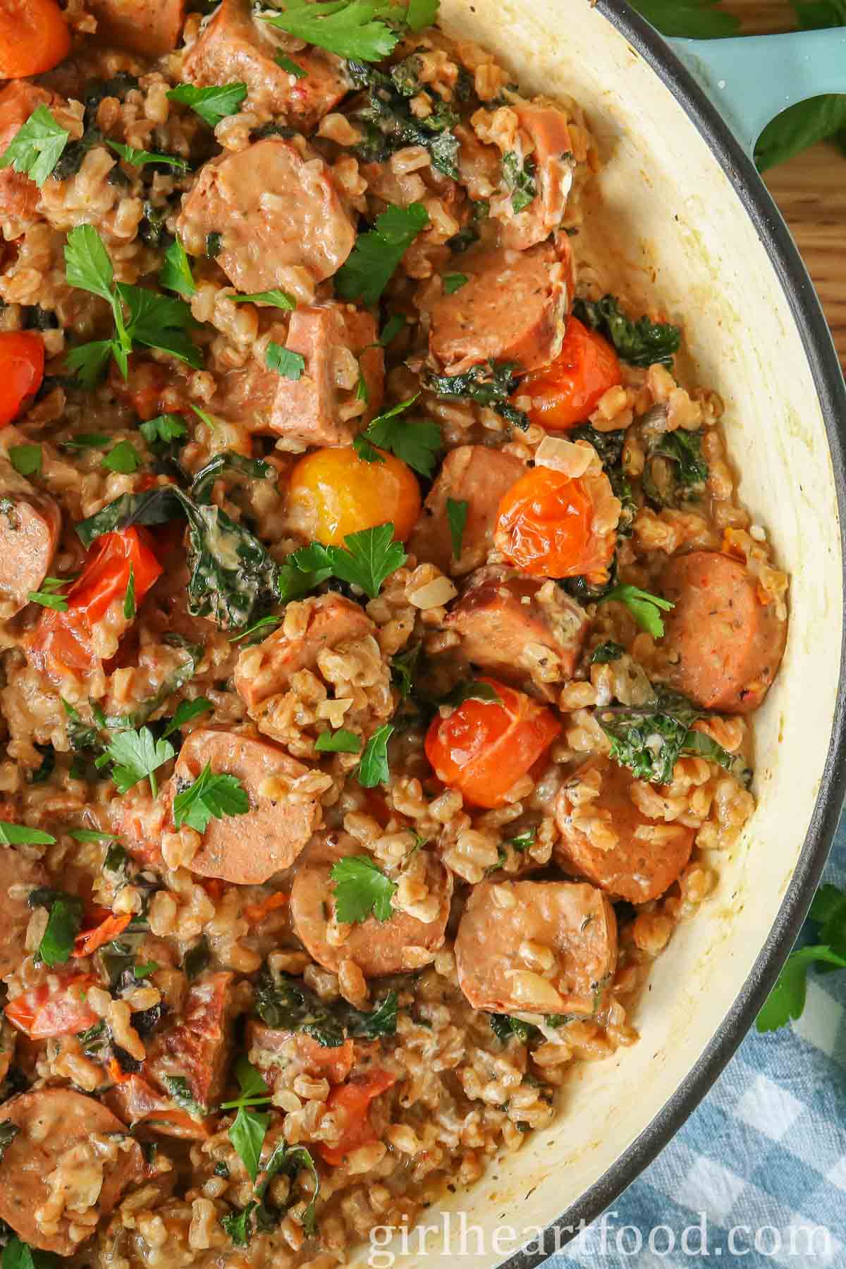 Close-up of a pan of sausage, farro and vegetables garnished with parsley.