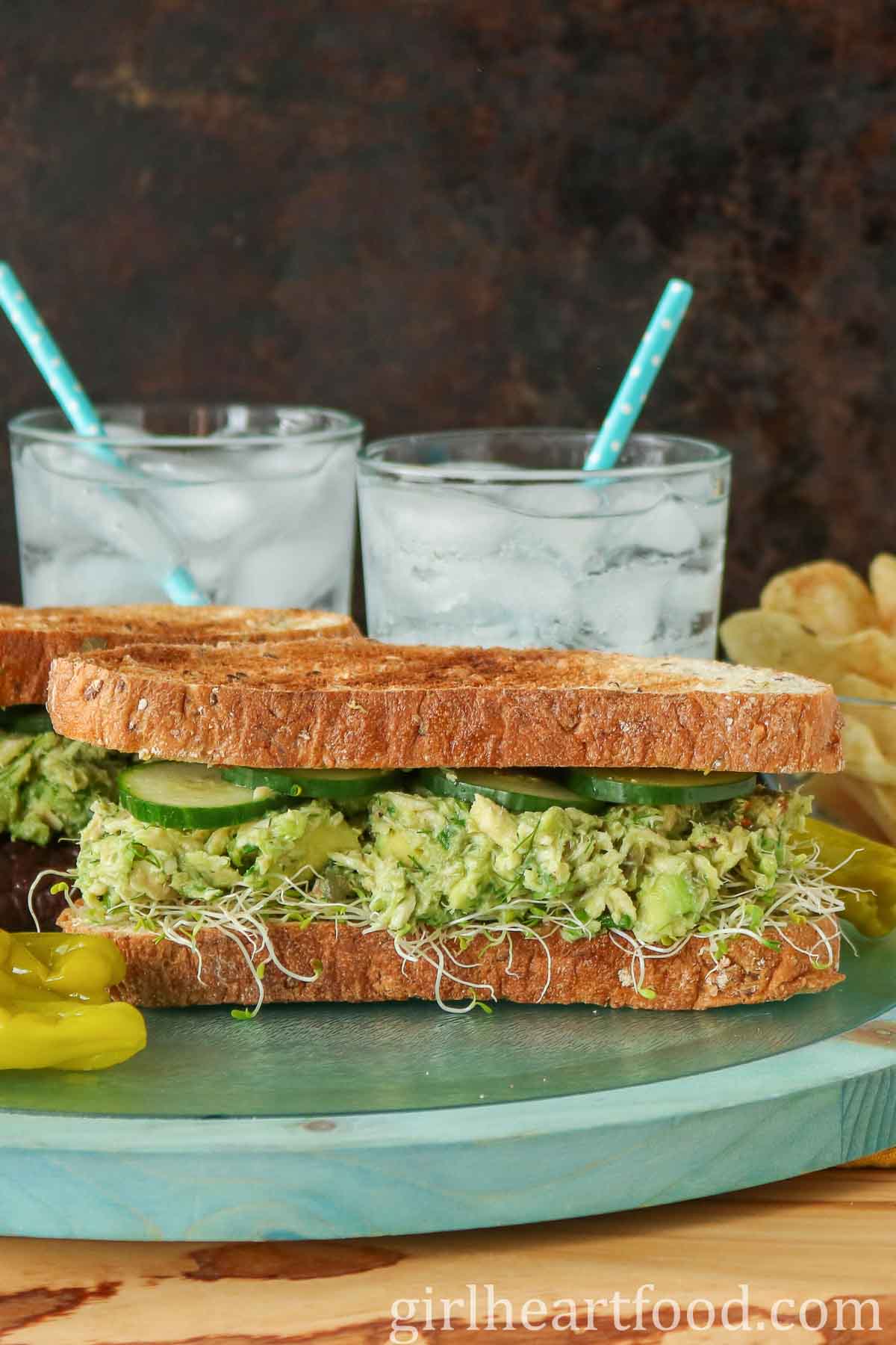 Two tuna avocado salad sandwiches with glasses of water behind them.