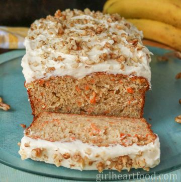 Cream cheese frosted loaf of carrot cake banana bread with a slice cut out of the loaf.