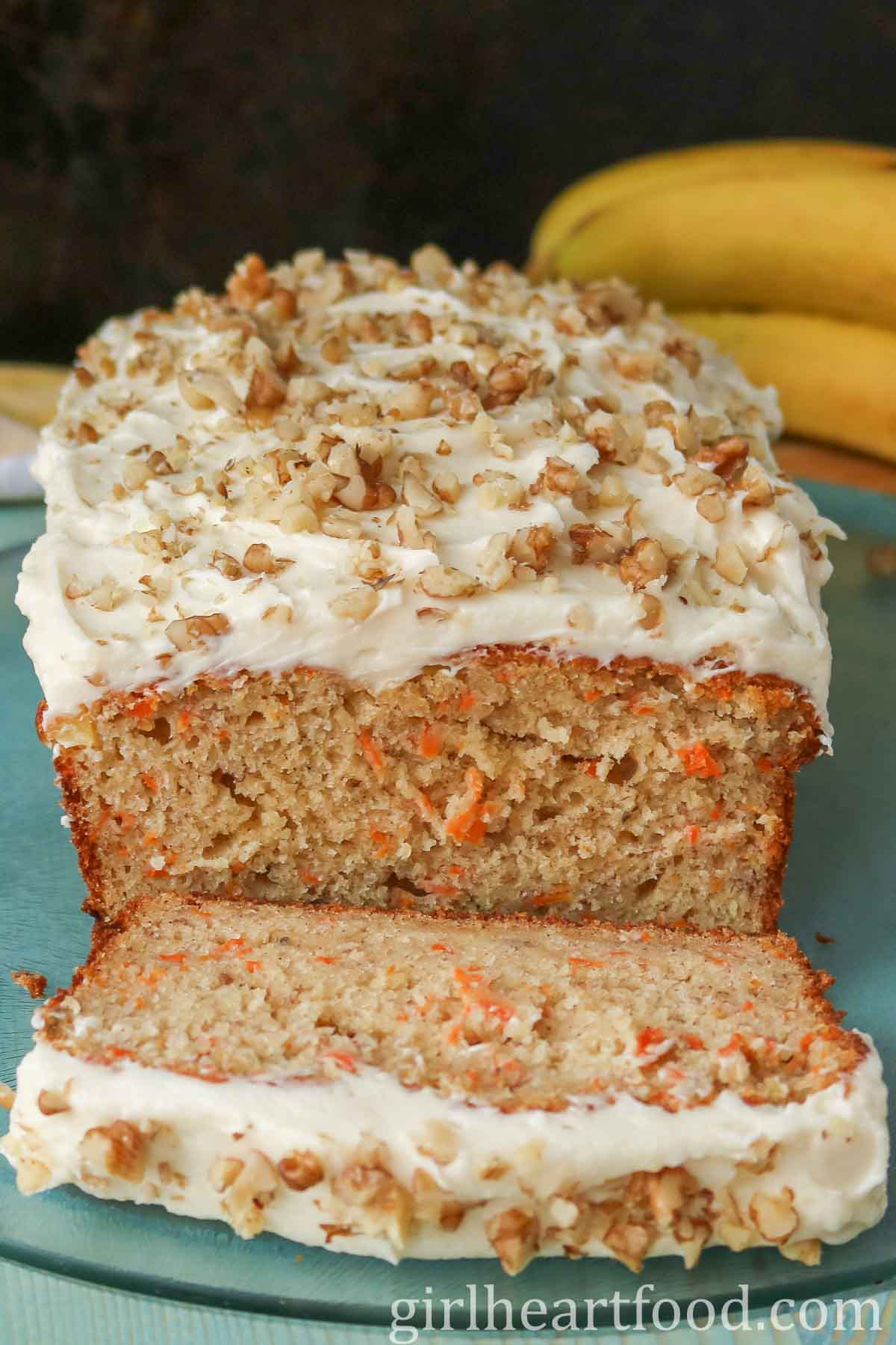 Cream cheese frosted carrot cake banana bread with a slice cut off.