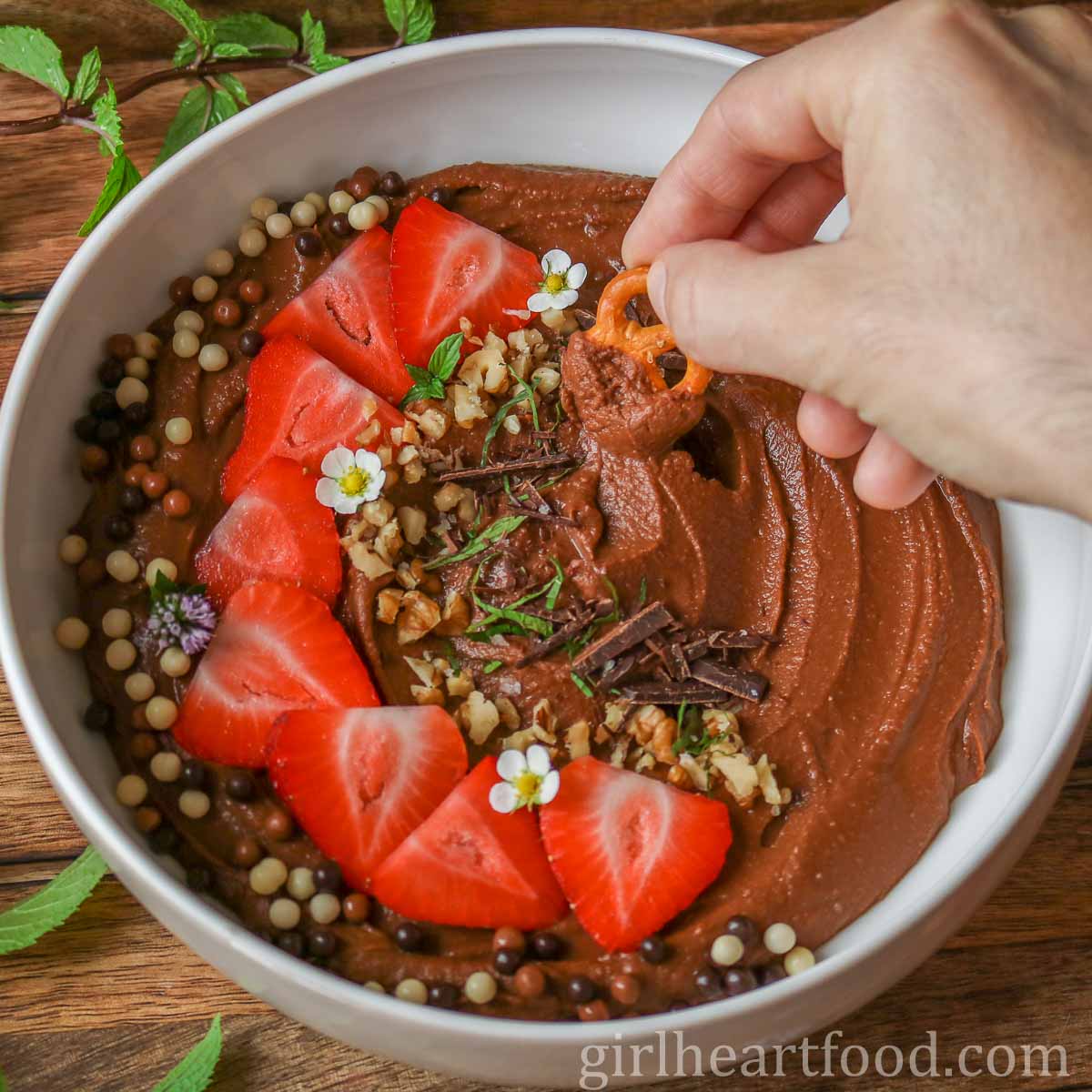 Hand dipping a pretzel into a bowl of sweet hummus.