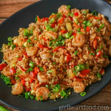 Homemade fried rice with shrimp, vegetables and pineapple on a black platter.