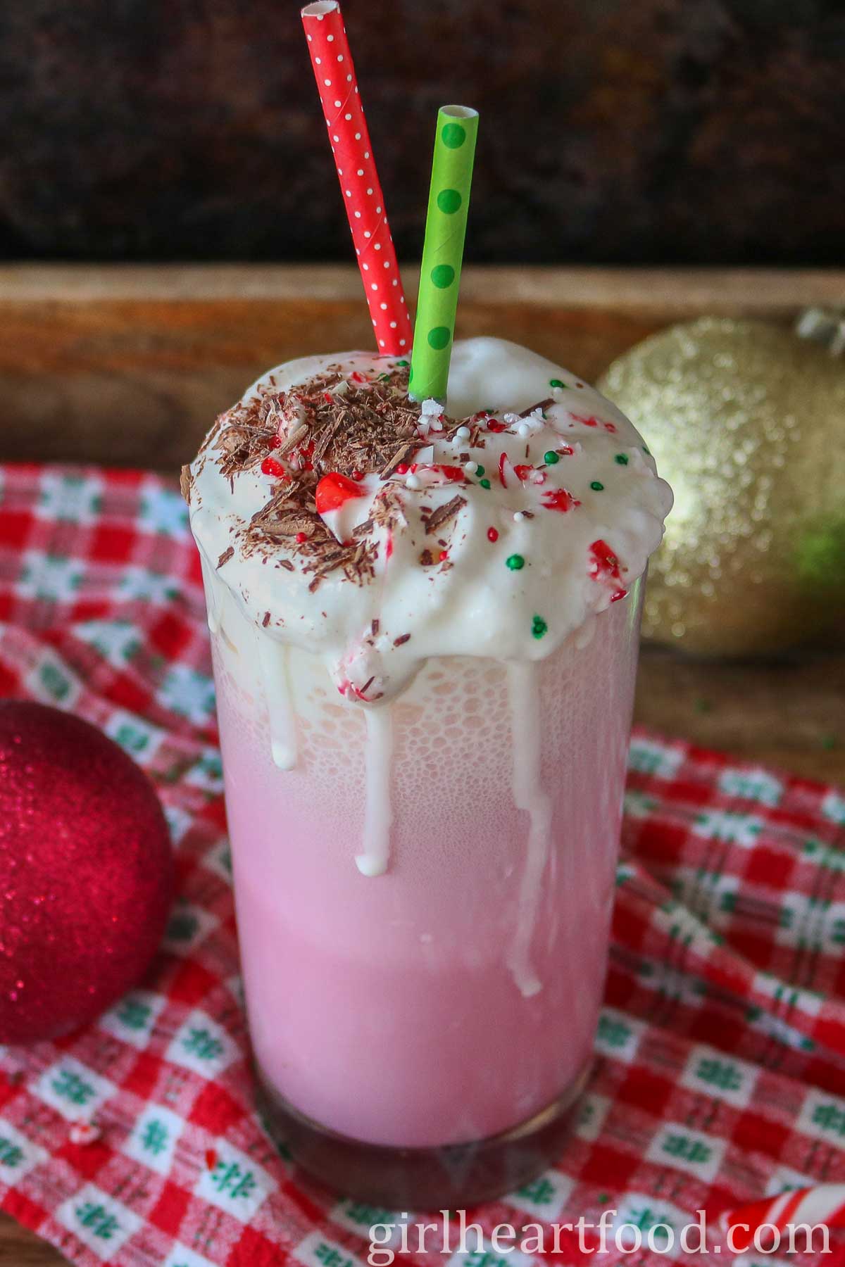 Glass of pink candy cane milkshake with milkshake spilling out over the top and down the glass.