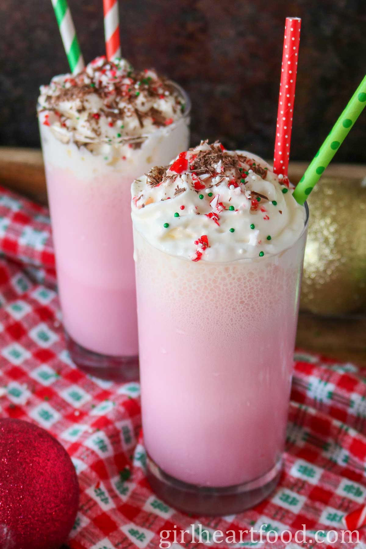 Two glasses of pink candy cane milkshake with whipped cream and toppings.