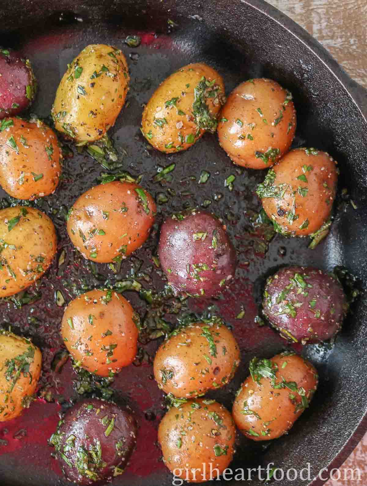 Baby potatoes with herbs in a cast-iron skillet before being roasted.