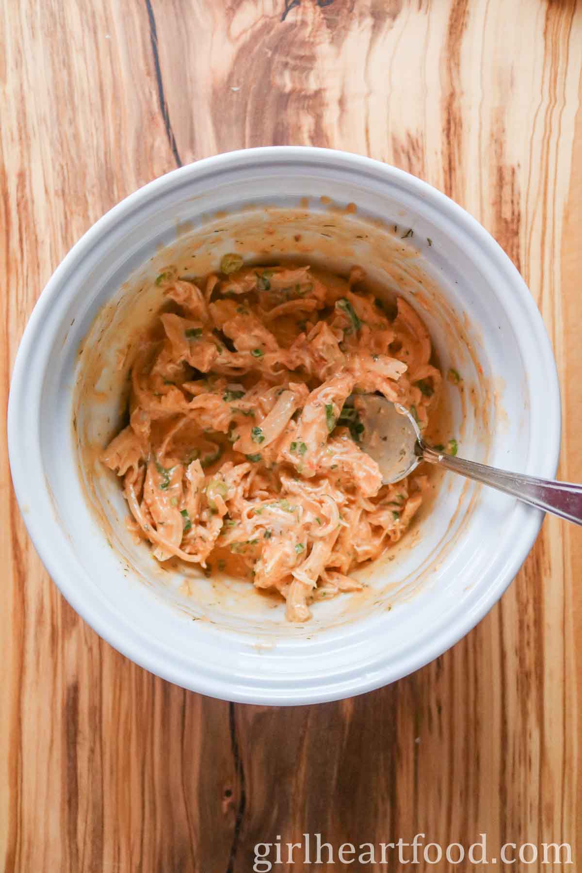 Buffalo chicken salad in a white bowl, with a spoon resting in the mixture.
