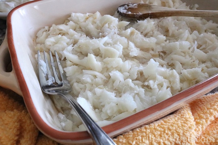 Cod in a casserole dish with a fork and wooden spoon resting on top.