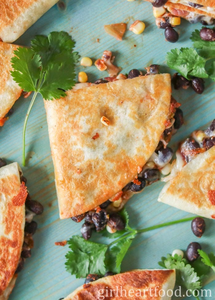 Black bean quesadillas on a blue board next to fresh cilantro.