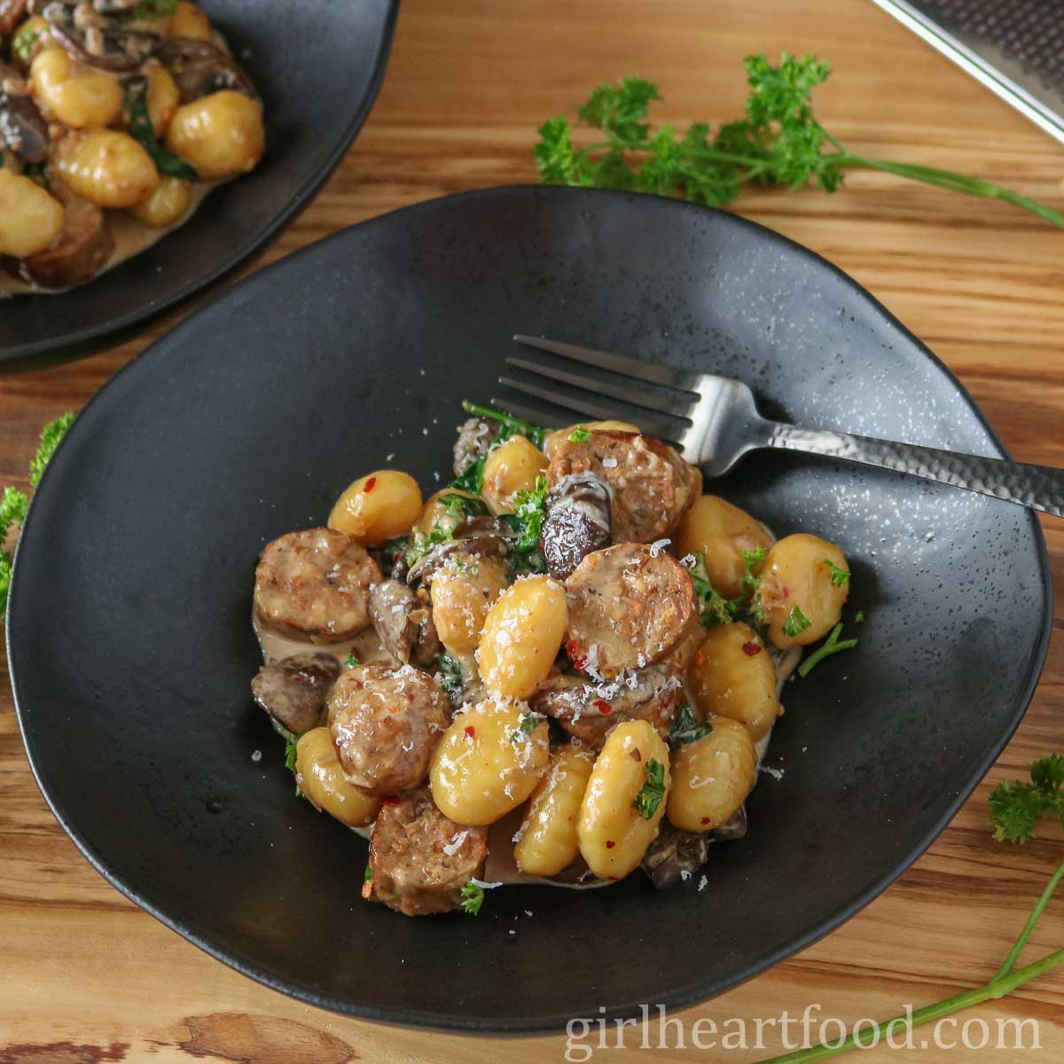 Bowl of sausage and gnocchi in cream sauce with a fork resting in the bowl.