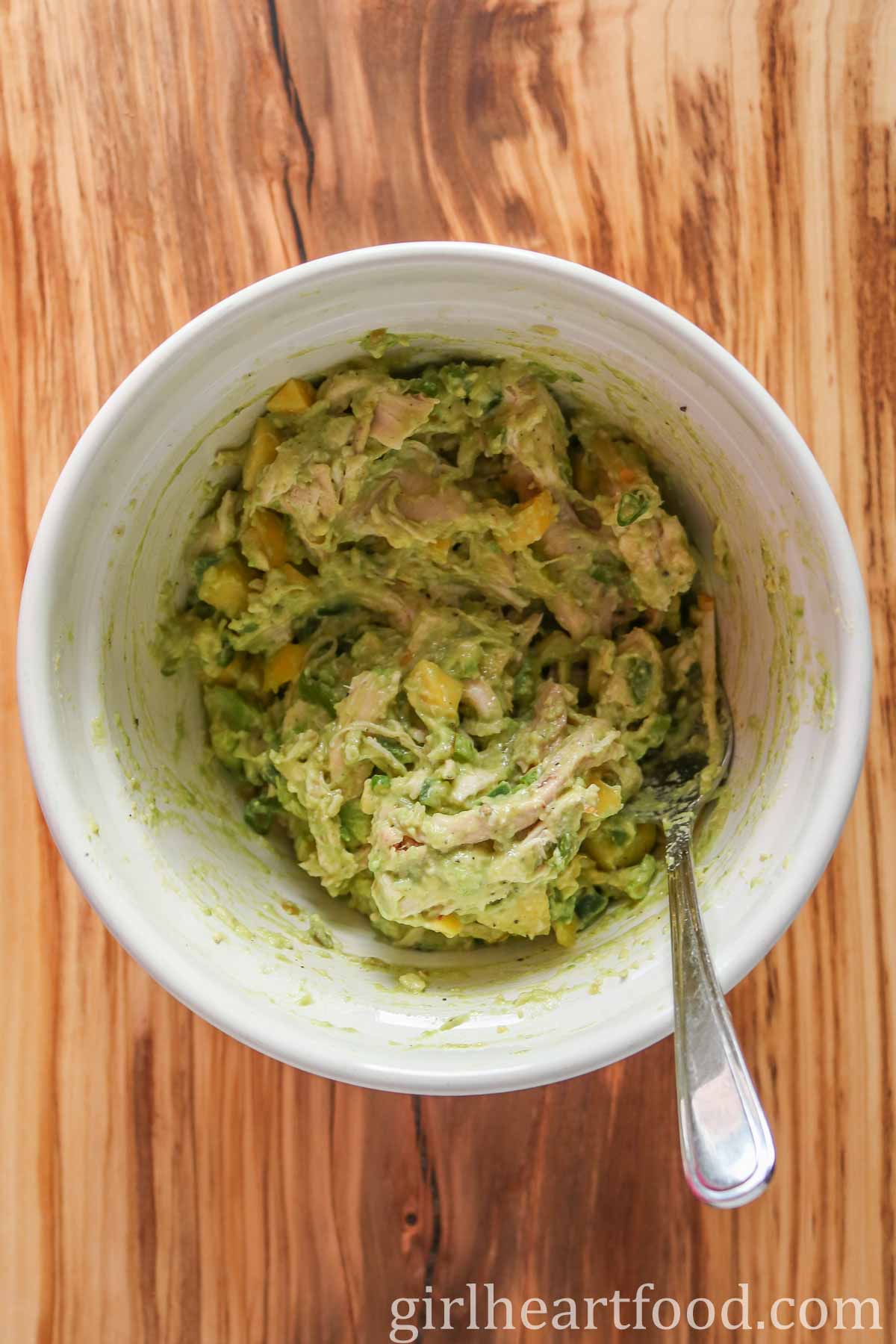 Chicken avocado salad mixture in a white bowl with a spoon resting in the mixture.