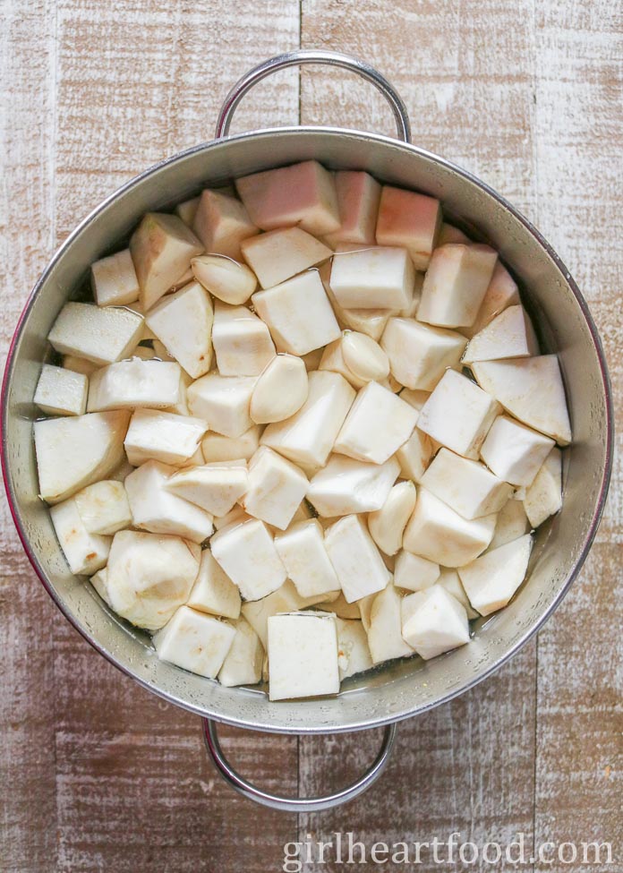 Cubes of uncooked celeriac and garlic cloves in a pot of water.