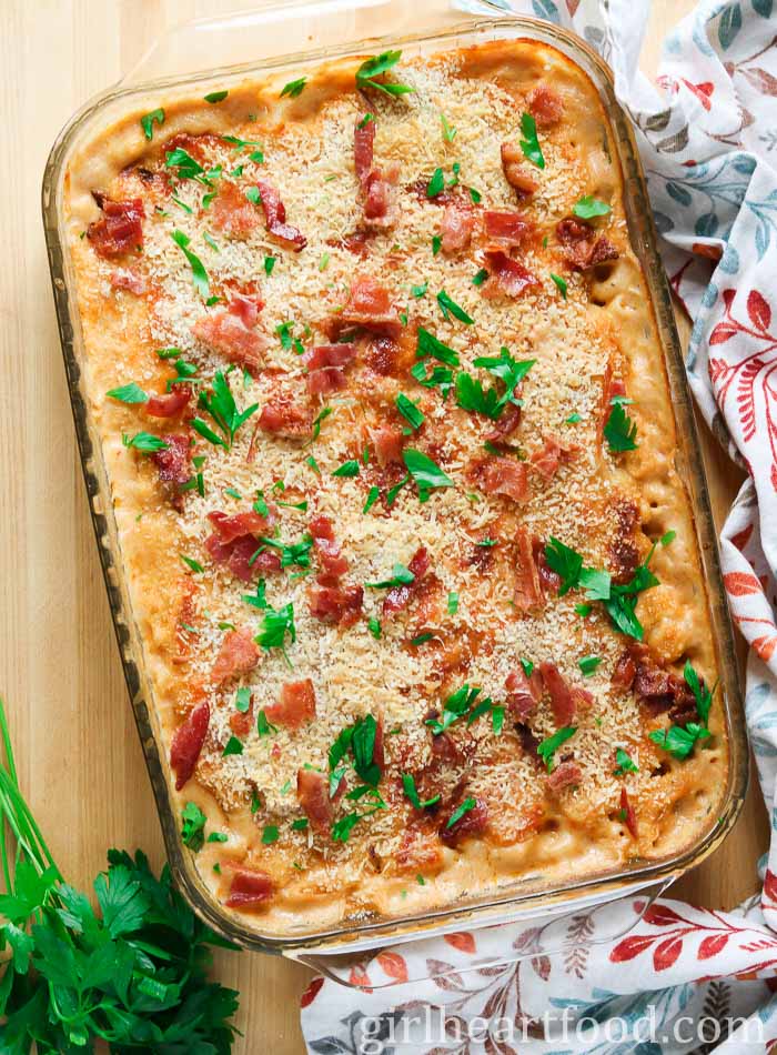 Baking dish of of creamy baked mac and cheese with parsley and crispy bacon pieces on top.