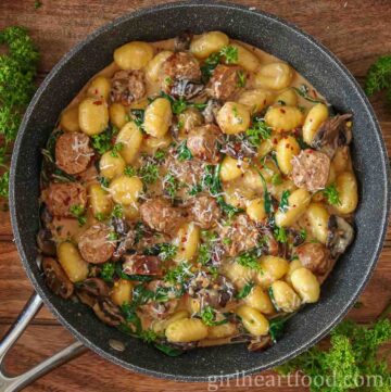 Pan of sausage, gnocchi, mushrooms and spinach with cream sauce next to fresh parsley.