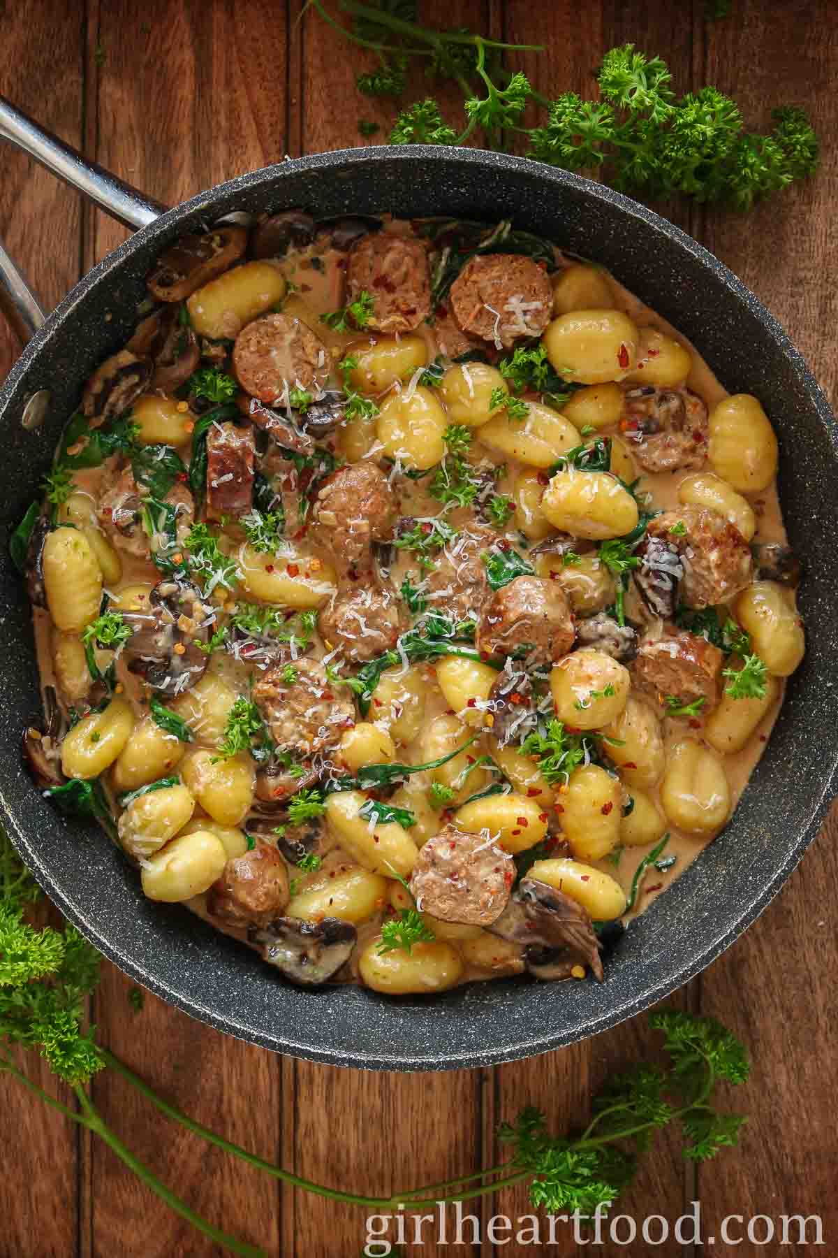 Pan of sausage, gnocchi, mushrooms and spinach in cream sauce next to fresh parsley.