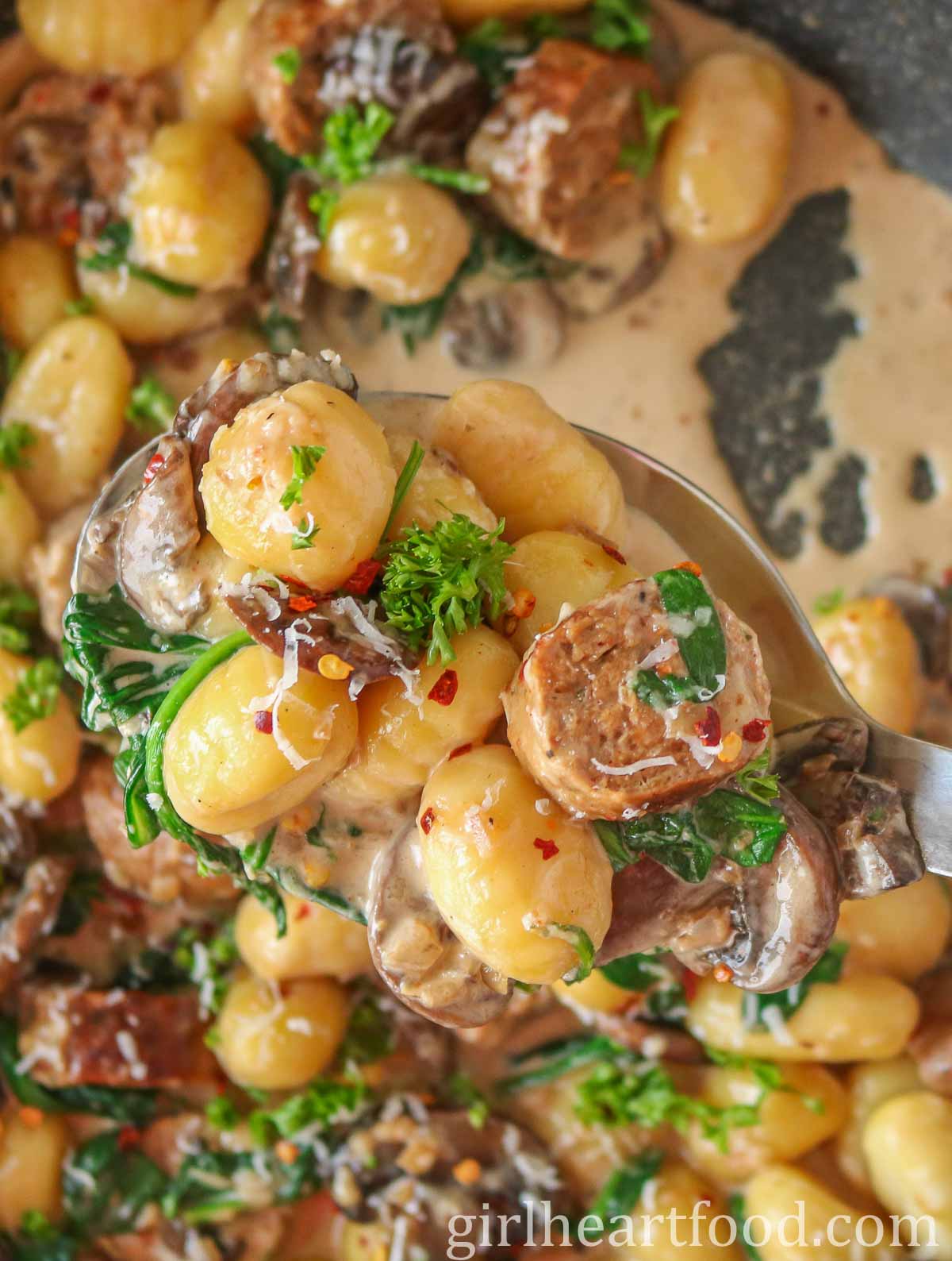 Serving spoon of sausage, gnocchi, mushrooms and spinach from a pan.