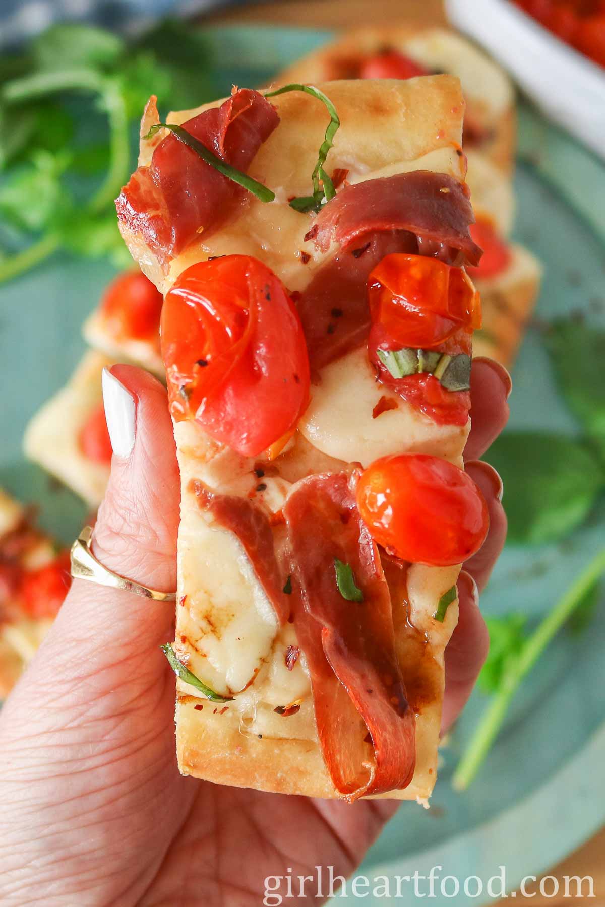Hand holding a piece of homemade flatbread pizza.