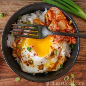 Fried egg (with the yolk broke) and rice bowl and a black fork resting on top.