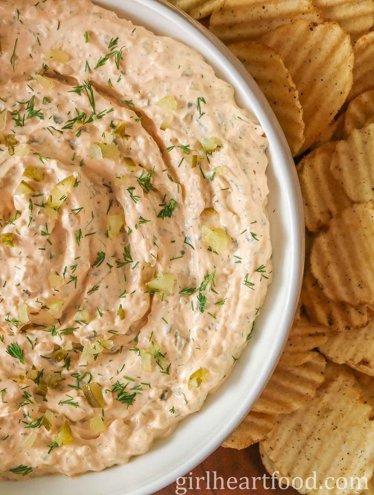 Close-up of a bowl of dill pickle dip alongside potato chips.