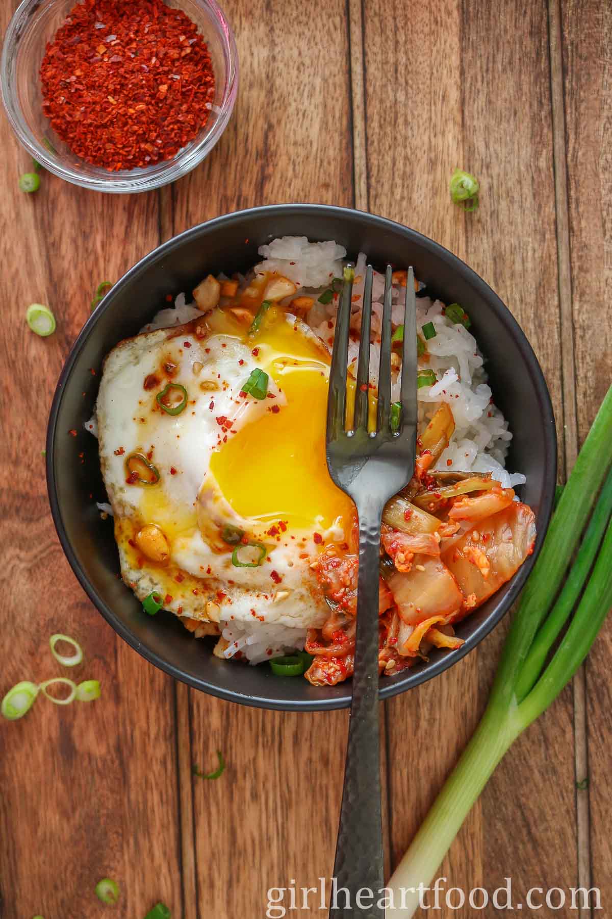 Fried egg (with the yolk broke) and rice bowl and a black fork resting on top.