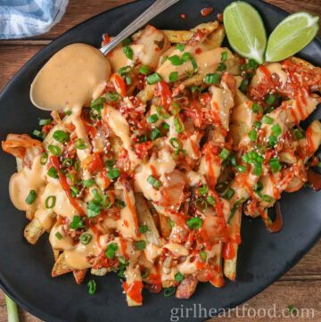 Cheesy kimchi fries, lime wedges and a spoon with cheese sauce on a platter.