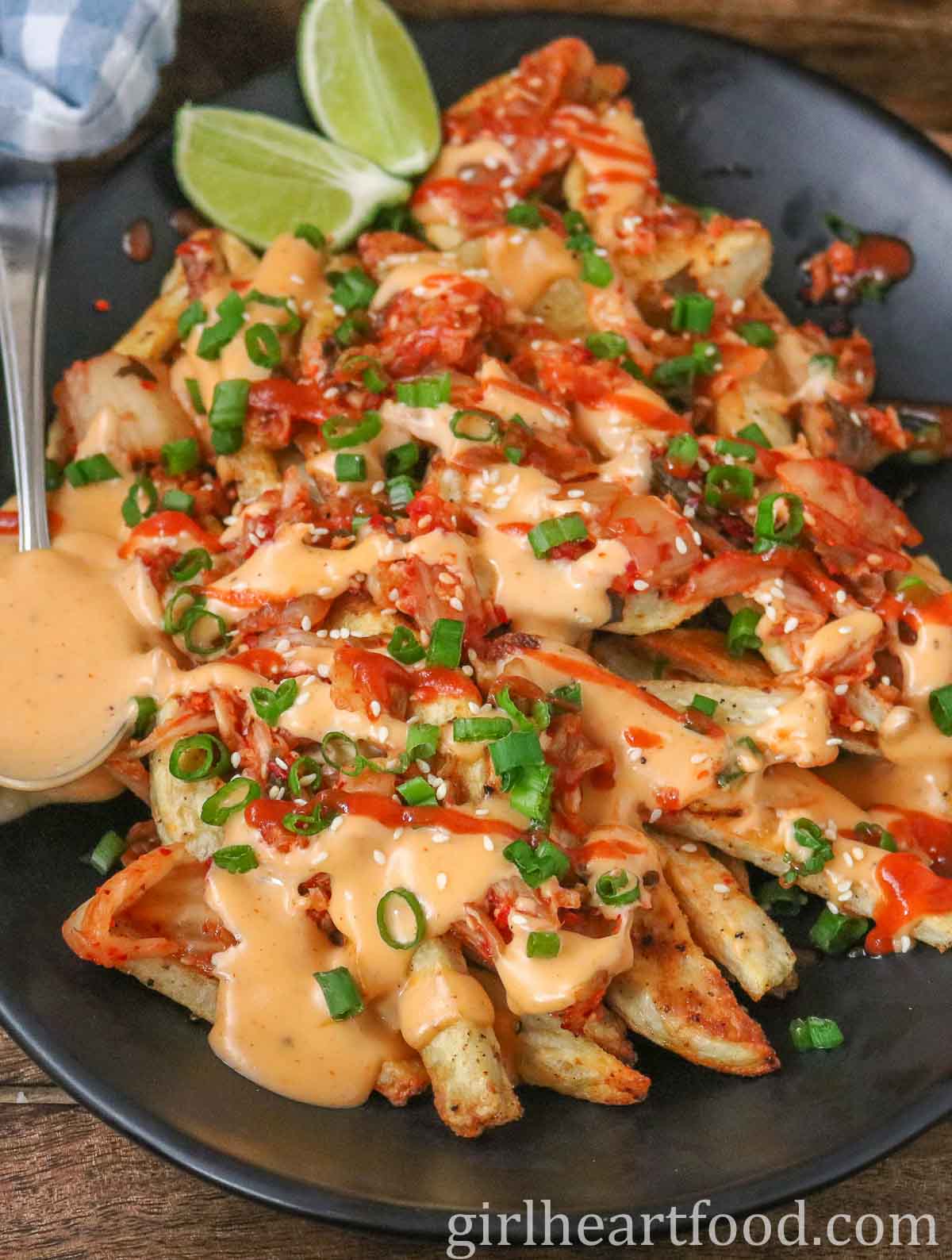 Kimchi fries with cheese sauce on a platter with a spoonful of cheese sauce alongside it.
