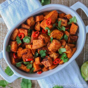 Roasted sweet potato chunks in a dish garnished with cilantro and chili pepper.